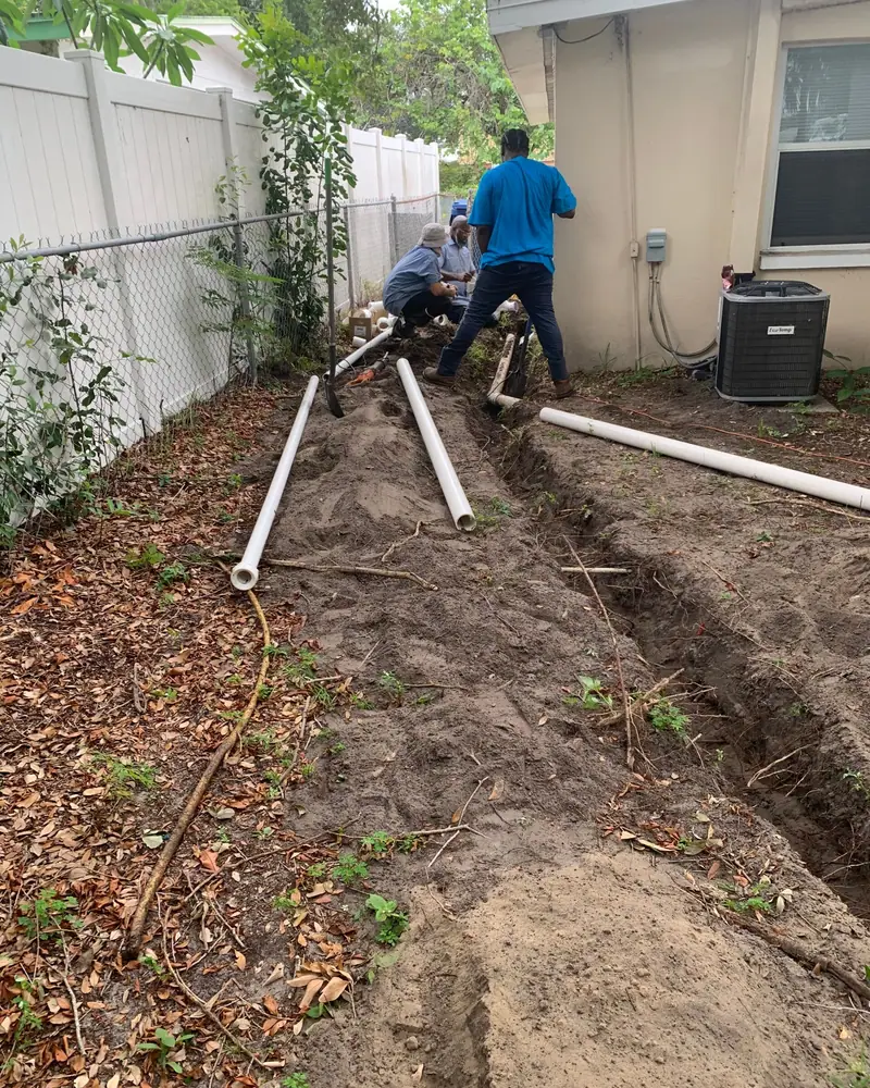 3 J's crew trenching a yard sewer line, new PVC laid out beside it