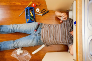 Plumber repairing pipes under a bathroom sink in a residential home